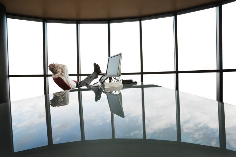 A businessman at his reflective office desk next to a large bank of windows.