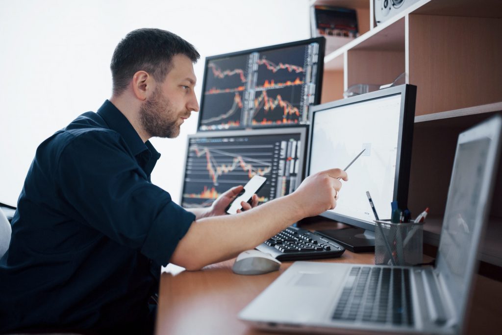 Stockbroker in shirt is working in a monitoring room with display screens. Stock Exchange Trading