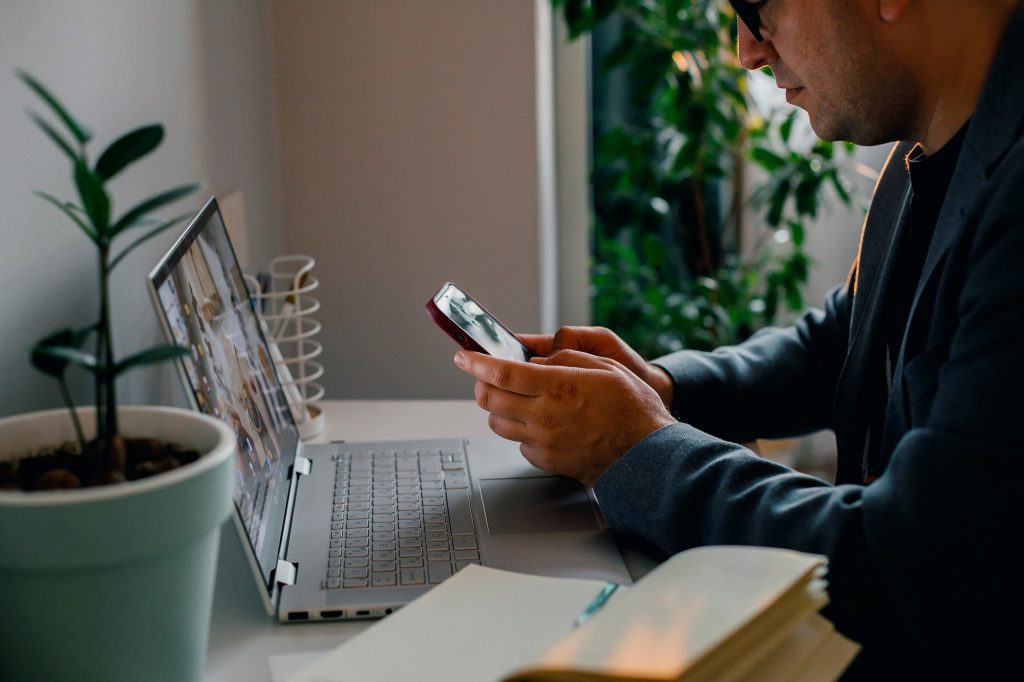 Young European man using phone while working in laptop .